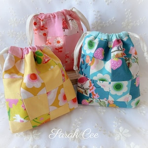 May include: Three drawstring bags with patchwork designs. One is yellow with floral patterns, another is pink with strawberries, and the third is blue with flowers and strawberries. Each bag has a white drawstring closure.
