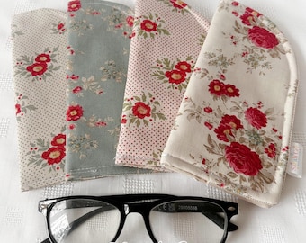 May include: Four fabric eyeglass cases with floral patterns in cream, blue, and pink, next to black-framed glasses. The cases have red rose designs. The items are arranged on a white surface.