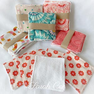May include: Several sets of reusable face cloths with diverse patterns, such as hearts, geometric shapes, and floral designs. Each set is bound with a brown paper band. The cloths feature pink, teal, and cream hues. The text "Sarah Cee" is visible.