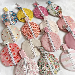 May include: A collection of 14 round zippered pouches in various colours and patterns. The pouches are made of fabric and have a zipper closure. The pouches are arranged in a circle on a white surface.