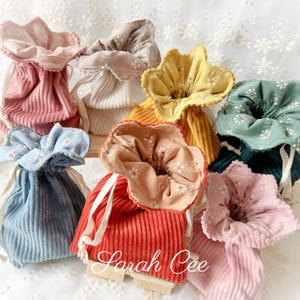 May include: A collection of small drawstring pouches made from ribbed corduroy fabric in various colours including blue, red, yellow, green, and pink. Each pouch features a floral patterned fabric lining that extends over the top edge and white cords.