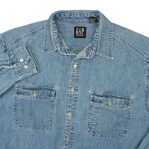 以下が含まれることがあります： GAP DENIMのライトブルーの長袖デニムシャツ。クラシックな襟、フロントボタン留め、ボタン付きの胸ポケットが2つ付いています。色あせたウォッシュ加工が施されており、明るい色のボタンと首元に黒いブランドラベルが付いています。