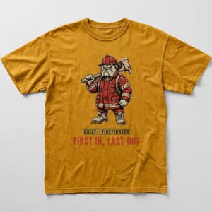 May include: A mustard yellow short-sleeve t-shirt featuring a graphic of a bulldog dressed as a firefighter, holding an axe. Below the graphic, the text reads CHIEF FIREFIGHTER and FIRST IN, LAST OUT in red and black lettering on the front centre.