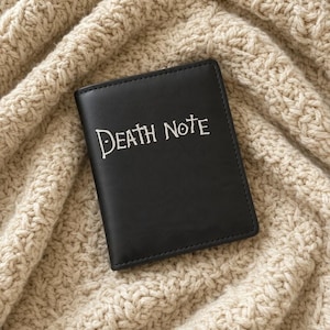 May include: A rectangular black notebook with a smooth finish featuring the white text Death Note printed on the front cover. The notebook has clean, straight edges and a simple, functional design for writing or note-taking purposes.
