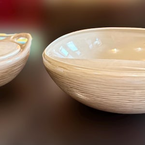 May include: A set of two beige ceramic bowls with a woodgrain pattern. The larger bowl is wider and shallower than the smaller bowl, which has a lid.