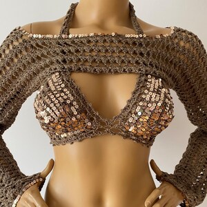 May include: A brown crochet top with long sleeves and a halter neckline. The top has a cutout in the front and is decorated with gold sequins. The top is paired with a matching brown crochet skirt.