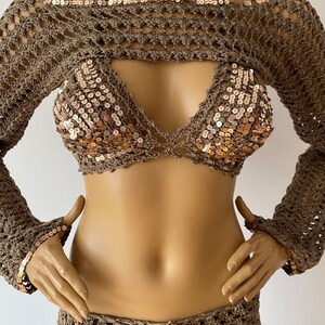 May include: A brown crochet top with long sleeves and a halter neckline. The top features a crocheted design with sequins. The top is worn over a matching brown crochet skirt.