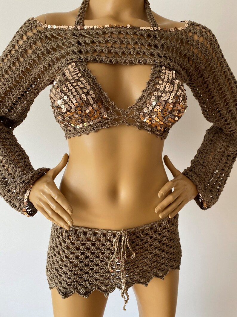 May include: A brown crochet top with long sleeves and a matching brown crochet skirt. The top has a halter neckline and a sequined bodice.