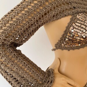 May include: A brown crochet top with long sleeves and a sequined bodice. The top has a cutout design in the front and is made of a delicate, open-weave fabric.
