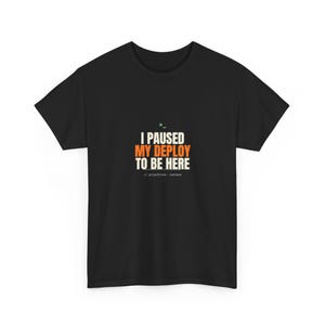 Könnte beinhalten: Ein schwarzes Kurzarm-T-Shirt mit dem weißen und orangefarbenen Text I PAUSED MY DEPLOY TO BE HERE. Über dem Text befindet sich ein kleines grünes Befehlszeilensymbol und unter dem Text der weiße Code-Kommentar // priorities::correct.