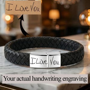 May include: A black braided leather bracelet featuring a rectangular silver-toned metal clasp. The clasp is engraved with the handwritten text I Love You, which matches the sample text shown on a tan rectangular card above the bracelet.