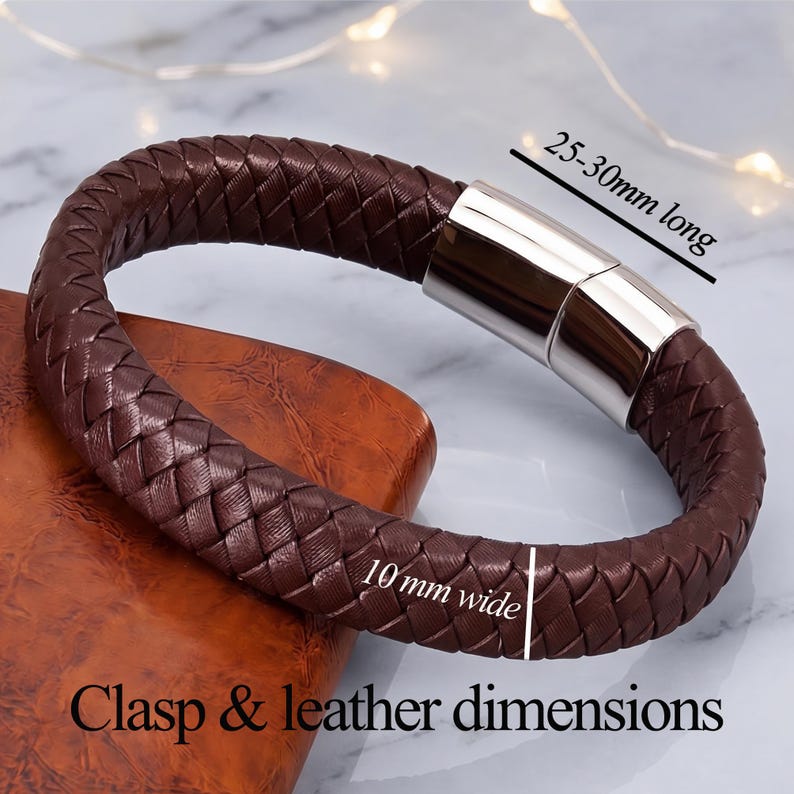 May include: A dark brown braided leather bracelet featuring a polished silver-tone metal magnetic clasp. The bracelet is 10 mm wide, and the clasp measures 25-30 mm long. The text "Clasp & leather dimensions" is visible at the bottom.