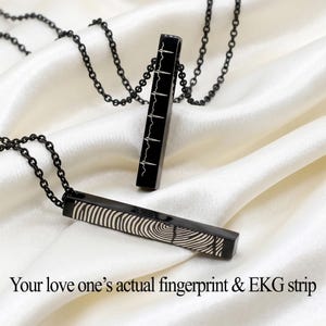 May include: Two black bar necklaces with chain links. One pendant features a fingerprint design, the other an EKG strip. The text reads: "Your love one's actual fingerprint & EKG strip."
