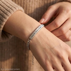 May include: A silver bracelet with a rectangular bar engraved with the words "Love Ya Pretty Gia" in a handwritten style. The bracelet features a curb chain and is being worn on a wrist.