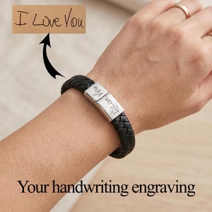 May include: A black braided leather bracelet featuring a silver-toned metal clasp engraved with the handwritten text I Love You. The design showcases a smooth rectangular metal centerpiece that displays the custom script clearly on its surface.