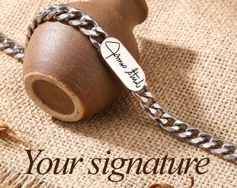 Puede incluir: Una pulsera de cadena de eslabones plateada con una placa rectangular con una firma manuscrita. La pulsera está colocada sobre un pequeño jarrón de cerámica marrón. El texto "Your signature" está en la parte inferior de la imagen.