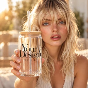 May include: A clear glass tumbler with a cylindrical shape, featuring a bamboo lid and a straight glass straw. The front of the glass is printed with the black text Your Design Here, positioned centrally in a serif font with a small arrow graphic.