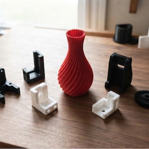 May include: A collection of 3D printed objects including a central red spiral vase, two black L-shaped brackets, two white L-shaped brackets, a black gear, and other small black and white plastic components arranged on a wooden surface.