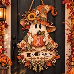 May include: A decorative wooden door hanger shaped like a ghost wearing a plaid witch hat, holding an orange pumpkin with a pink awareness ribbon. Below, a rectangular sign reads THE SMITH FAMILY, accented with autumn leaves and a plaid bow.