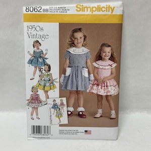 Puede incluir: Patrón de costura Simplicity 8062 BB para vestidos infantiles en tallas 4, 5, 6, 7 y 8. El sobre presenta ilustraciones y fotografías de vestidos con cuadros vichy, estampados florales, cuellos marineros y bolsillos, etiquetado 1950s Vintage.