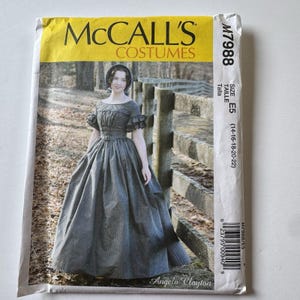May include: A McCall's Costumes sewing pattern envelope M7988, size E5 (14-16-18-20-22), featuring a photograph of a person wearing a dark, floor-length, short-sleeved dress with a gathered bodice and a full skirt, designed by Angela Clayton.
