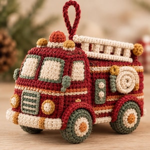 May include: A crocheted fire truck ornament in deep red, cream, and muted green yarn. The vehicle features a cream-colored ladder on top, a coiled hose on the side, a red light on the roof, and a hanging loop made of matching red yarn.