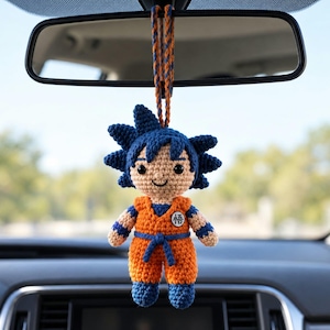Könnte beinhalten: Eine gehäkelte Puppe eines Charakters mit stacheligem dunkelblauem Haar, bekleidet mit einem orange-blauen Gi mit einem weißen kreisförmigen Emblem, das das schwarze Kanji-Zeichen Go zeigt, aufgehängt an einer orange-blauen Kordel.