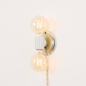 May include: A white ceramic wall sconce with a gold metal base and two clear glass light bulbs.