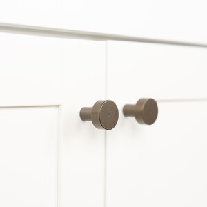Op de afbeelding: Twee ronde, bronzen kastknoppen met een licht getextureerde afwerking.