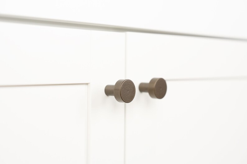 Op de afbeelding: Twee ronde, bronzen kastknoppen met een licht getextureerde afwerking.