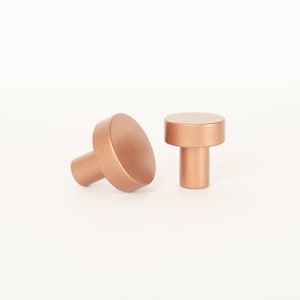 May include: Two round, copper-colored cabinet knobs with a smooth, matte finish.