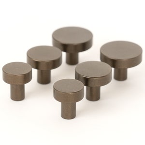 Op de afbeelding: Zes kleine, ronde, bronzenkleurige kastknoppen met een glad, licht getextureerd oppervlak. De knoppen hebben een korte, cilindrische steel.