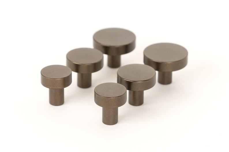 Op de afbeelding: Zes kleine, ronde, bronzenkleurige kastknoppen met een glad, licht getextureerd oppervlak. De knoppen hebben een korte, cilindrische steel.