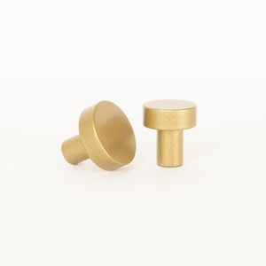 May include: Two gold-toned cabinet knobs with a round top and a cylindrical base.