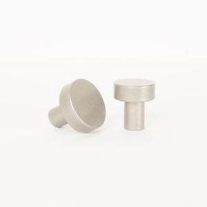 May include: Two silver metal cabinet knobs with a round top and a cylindrical base.