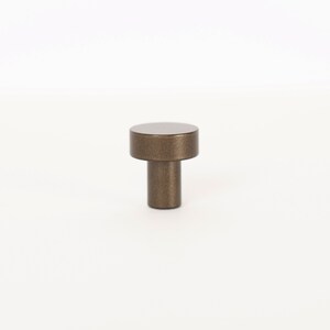 Op de afbeelding: Een kleine, ronde, bronzen kastknop met een textuur.