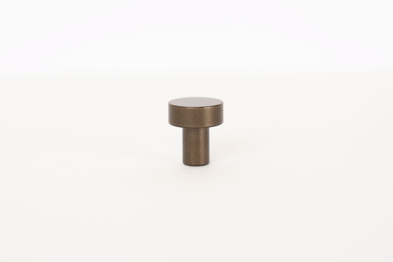 Op de afbeelding: Een kleine, ronde, bronzen kastknop met een textuur.