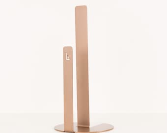 May include: A gold metal paper towel holder with a simple design. The holder has a rectangular base and two vertical bars that hold the paper towel roll.