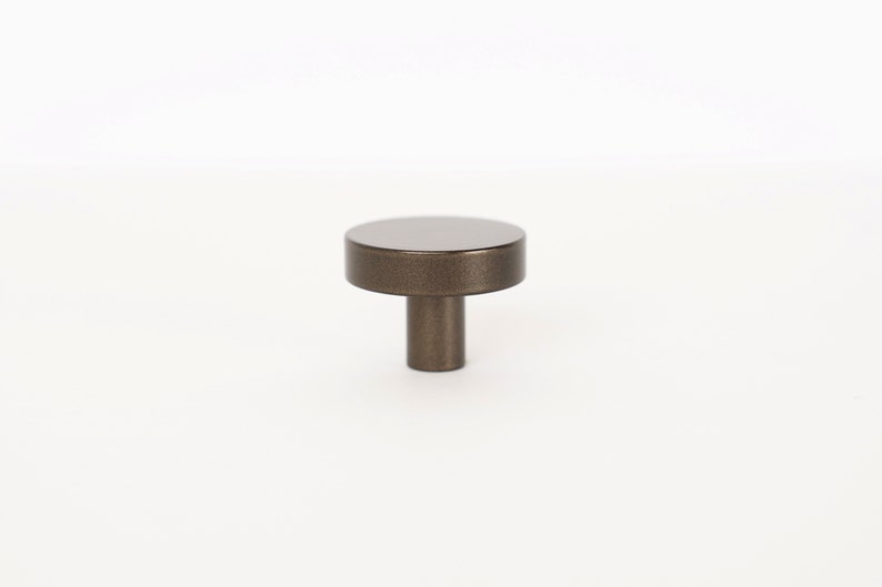 Op de afbeelding: Een ronde, bronzen kastknop met een korte, cilindrische steel.