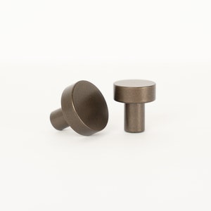 May include: Two round, bronze cabinet knobs with a cylindrical base.