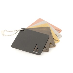 May include: A set of five metal color swatches attached to a silver chain. The swatches are in shades of black, gray, gold, copper, and rose gold.