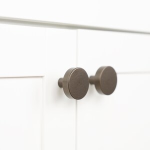 Op de afbeelding: Twee ronde, geborstelde nikkel kastknoppen met een licht getextureerde afwerking.