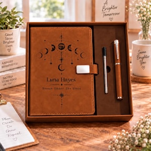 May include: A tan leather-like journal with a moon phase graphic, the name Luna Hayes, and the text Dream Under The Stars, paired with a matching pen in a presentation box. The journal features a silver-toned magnetic closure tab.