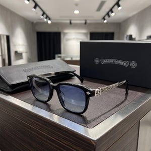 Puede incluir: Gafas de sol con montura negra, lentes degradadas en azul y patillas de metal plateado con grabados florales intrincados. Las gafas vienen con un estuche de cuero negro y una caja negra, ambos con el logotipo de Chrome Hearts impreso.