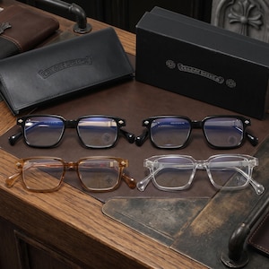 May include: Four pairs of rectangular eyeglasses with Chrome Hearts branding on the frames and lenses. The collection includes two black frames, one translucent amber frame, and one clear frame, accompanied by a black leather case and a black box.