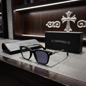 Puede incluir: Gafas de montura negra con patillas de metal plateado que presentan intrincados detalles decorativos. Las gafas vienen acompañadas de un estuche de textura de cuero negro y una caja rectangular negra con el logo de Chrome Hearts en plata.