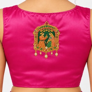 May include: A sleeveless fuchsia blouse featuring a central rectangular embroidered patch. The patch depicts two figures in traditional attire within a gold-toned ornate frame, accented with green, red, and white beads and dangling pearls.