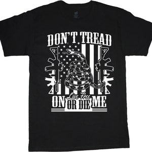 May include: Black t-shirt with a white graphic design featuring a snake wrapped around a stylized American flag with the text "Don't Tread On Or Die Me" and "Live Free" in the center.