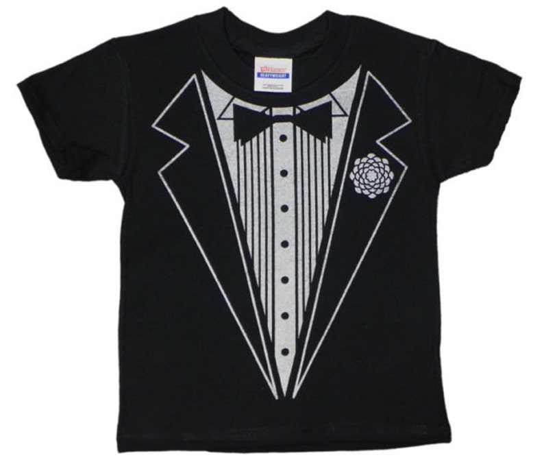 May include: Black t-shirt featuring a silver graphic of a tuxedo. The tuxedo has a bow tie and a flower on the lapel.