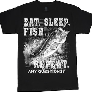 Pode incluir: Camiseta preta com um gráfico de um robalo saltando para fora da água. O texto "EAT. SLEEP. FISH... REPEAT. ANY QUESTIONS?" está impresso em letras brancas acima e abaixo do peixe.
